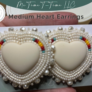Könnte beinhalten: Paar mittelgroße Herzohrringe. Jeder Ohrring hat eine cremefarbene Herzform, die von weißen Perlen umgeben ist. Akzente aus roten, gelben und blauen Perlen sind sichtbar. Der Text "Medium Heart Earrings" wird angezeigt.