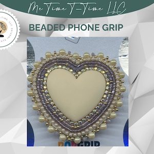May include: A heart-shaped phone grip featuring a smooth cream-colored center surrounded by concentric rows of iridescent lavender beads, sparkling clear crystals, and a final outer border of round cream-colored beads on a white backing.