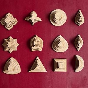 May include: A collection of twelve laser-cut wooden shapes in various designs, including floral, geometric, and teardrop forms. The shapes are arranged on a red background, showcasing their layered construction and natural wood grain.