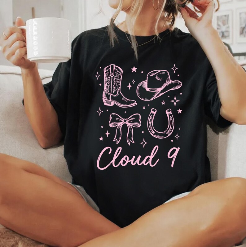 May include: Black t-shirt with a pink graphic featuring a cowboy boot, hat, bow, and horseshoe. The text "Cloud 9" is below the graphics. The shirt is a casual style.