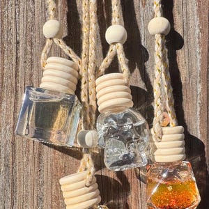 May include: Several small, clear glass bottles with wooden tops and hanging cords. The bottles contain colorful liquids and are suspended against a wooden background. The bottles have different shapes and contain various colors.