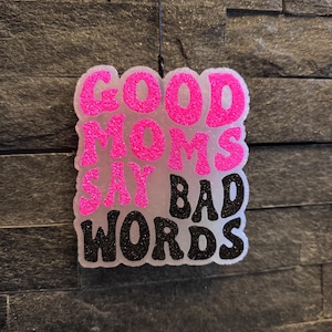Op de afbeelding: Een roze en zwarte autoluchtverfrisser met de tekst "GOOD MOMS SAY BAD WORDS".