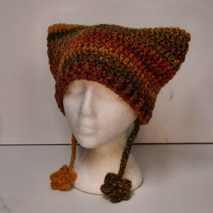 Può includere: Un cappello all'uncinetto con le alette per le orecchie e decorazioni floreali. Il cappello è realizzato in tonalità di marrone, arancione e verde.