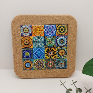 Pode incluir: Base de cortiça quadrada com um design de azulejos coloridos. A base apresenta uma grelha de dezasseis azulejos quadrados, cada um com um padrão único em tons de azul, amarelo, laranja e verde. A palavra "Portugal" está impressa no canto inferior direito.