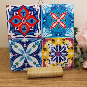 May include: A ceramic tile with a colorful Portuguese tile pattern. The tile is mounted on a wooden stand and has the word "Portugal" printed on it.
