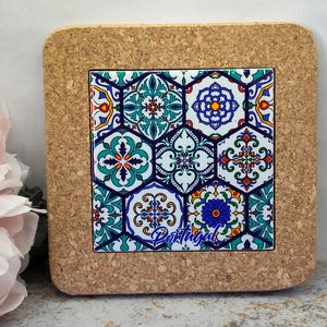 Pode incluir: Um porta-copos quadrado de cortiça com um azulejo de cerâmica central apresentando um padrão hexagonal colorido em azul, verde, amarelo e vermelho. O azulejo exibe motivos florais e geométricos, com a palavra Portugal escrita em azul abaixo.