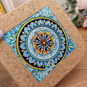 May include: Cork coaster with a blue and yellow tile featuring a circular design with the word "Portugal" in the bottom right corner.
