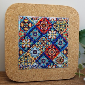 Puede incluir: Posavasos de corcho con un diseño de azulejos coloridos con motivos geométricos azules, rojos, amarillos y blancos. El diseño de los azulejos tiene la palabra "Portugal" impresa.