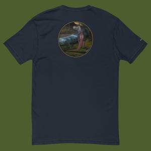 Könnte beinhalten: Marineblaues T-Shirt mit einem kreisförmigen Aufdruck auf dem Rücken. Der Aufdruck zeigt einen Dinosaurier in einer natürlichen Umgebung mit einem Fluss und Bäumen. Der Dinosaurier ist hauptsächlich rosa und grau. Das T-Shirt hat kurze Ärmel und einen Rundhalsausschnitt.