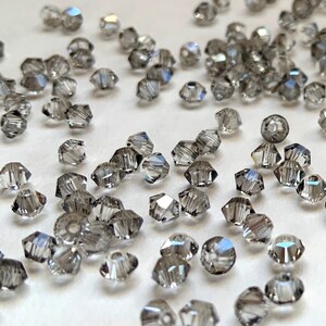 May include: A scattering of small, clear glass beads with a faceted, hexagonal shape. The beads have a subtle, iridescent shimmer.