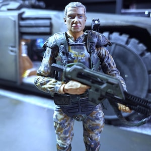 May include: A camouflage-patterned action figure of a soldier holding a futuristic weapon. The figure has a detailed face and is wearing a helmet and body armor.