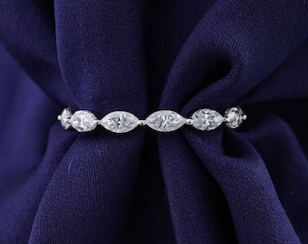May include: A delicate silver ring featuring a series of marquise-cut clear gemstones. The ring is set against a deep blue fabric, highlighting the sparkle of the stones. The gemstones are evenly spaced around the band.