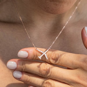 Può includere: Una collana in oro rosa con un piccolo ciondolo a forma di aereo incastonato con pietre di zircone cubico trasparenti.