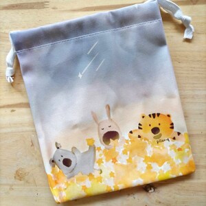May include: A grey drawstring bag with a white and yellow design. The design features three animals: a rabbit, a tiger, and a dog. The animals are surrounded by yellow stars. The bag has a white drawstring.