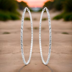 May include: A pair of silver hoop earrings with a textured finish. The earrings are large and circular in shape.