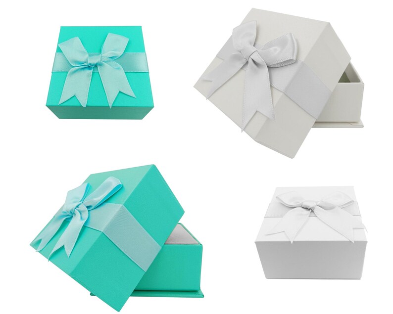 Puede incluir: Se muestran cuatro cajas de regalo. Dos son turquesas con cinta y lazo a juego, y dos son blancas con cinta y lazo plateados. Una caja turquesa est&aacute; abierta, revelando un interior blanco.