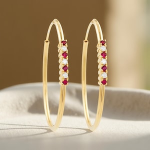 May include: A pair of gold hoop earrings with a row of red and white gemstones.
