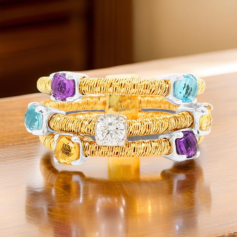 May include: A gold ring with a woven band and five gemstones. The gemstones are a round diamond, a square amethyst, a square topaz, a square citrine, and a square aquamarine.