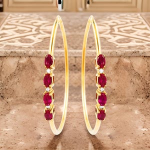 以下が含まれることがあります： ゴールドのフープイヤリング。各イヤリングに赤いルビーの宝石が5つと小さなクリアダイヤモンドがいくつか付いています。