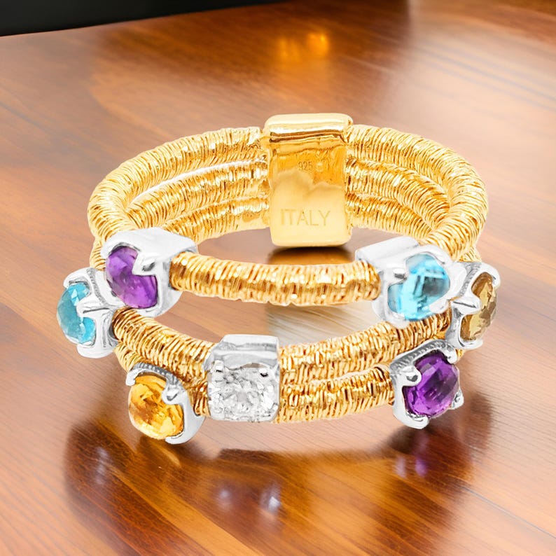 May include: A gold ring with multiple bands and colourful gemstones, including amethyst, topaz, and citrine. The ring is made in Italy.