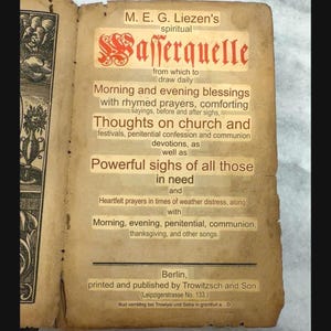 Puede incluir: Una página de libro antigua con papel envejecido y amarillento que presenta texto impreso en negro y rojo. El título dice M. E. G. Liezen's spiritual Wasserquelle, seguido de descripciones de bendiciones, oraciones y devociones.