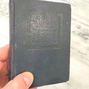 Può includere: Un piccolo libro con copertina rigida blu scuro e rivestimento in tessuto testurizzato. La copertina presenta la scritta dorata in rilievo "GOD'S MINUTE" racchiusa in un bordo rettangolare. Il libro ha il dorso usurato e bordi sfilacciati.