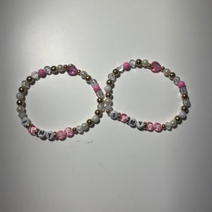 May include: Two beaded bracelets with gold beads, pink beads, and white beads. One bracelet spells "I love my BF" and the other spells "I love my GF".