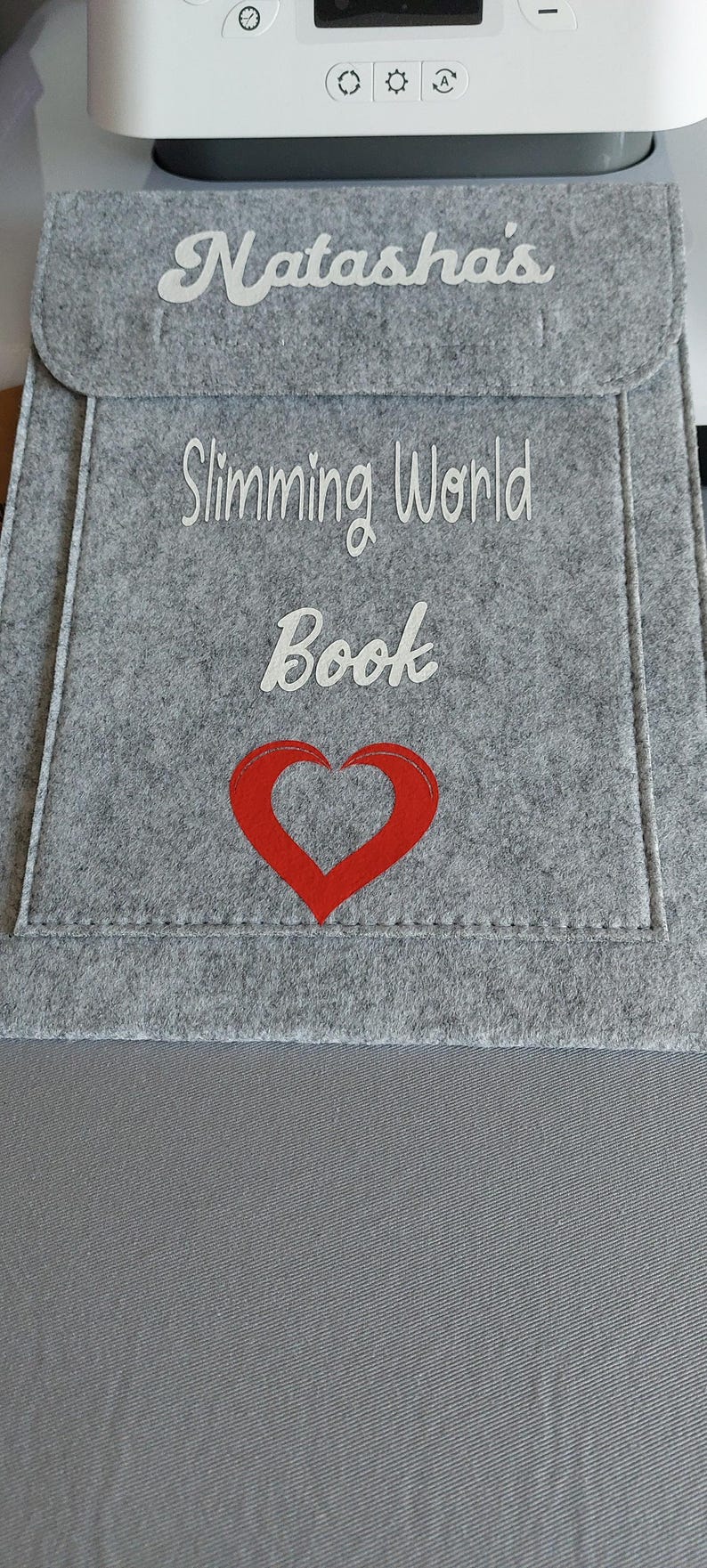 May include: Gray felt pouch with white embroidery that reads "Natasha's Slimming World Book" and a red heart.