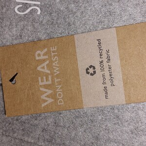 May include: A brown paper tag with the text "Wear Don't Waste" and a recycling symbol. The tag also says "made from 100% recycled polyester fabric" and "BagBase bagbase.com".