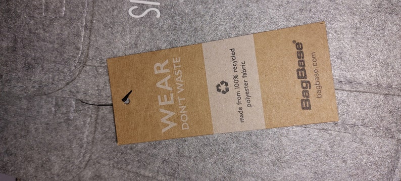 May include: A brown paper tag with the text "Wear Don't Waste" and a recycling symbol. The tag also says "made from 100% recycled polyester fabric" and "BagBase bagbase.com".