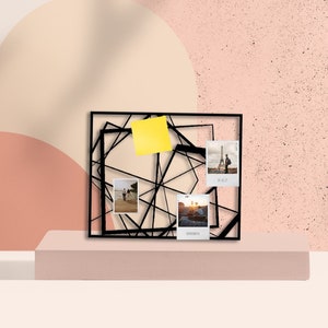 Può includere: Espositore per foto in metallo nero con un design geometrico. Ha quattro foto e un post-it giallo.