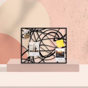 Può includere: Espositore per foto in metallo nero con un design geometrico. Il display ha quattro foto e un post-it giallo.