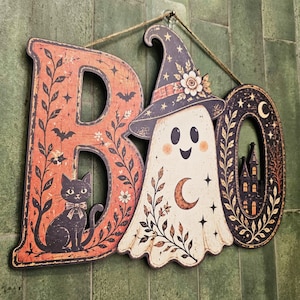May include: A decorative wall sign spelling the word BOO, featuring a black cat on the letter B, a ghost wearing a star-patterned witch hat in place of the letter O, and a haunted house silhouette inside the final letter O with twine.