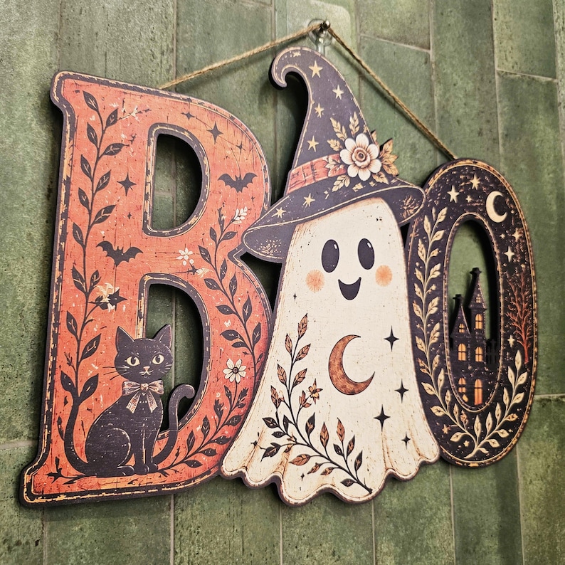 May include: A decorative wall sign spelling the word BOO, featuring a black cat on the letter B, a ghost wearing a star-patterned witch hat in place of the letter O, and a haunted house silhouette inside the final letter O with twine.