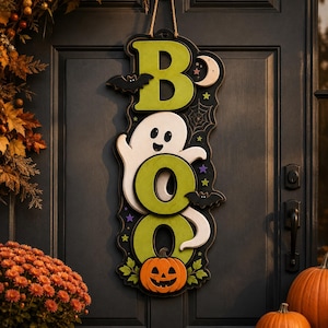 May include: A vertical hanging sign featuring the word BOO in large green letters. A white ghost is positioned between the letters, accompanied by black bats, a crescent moon, small stars, a spider web, and an orange jack-o'-lantern at the base.