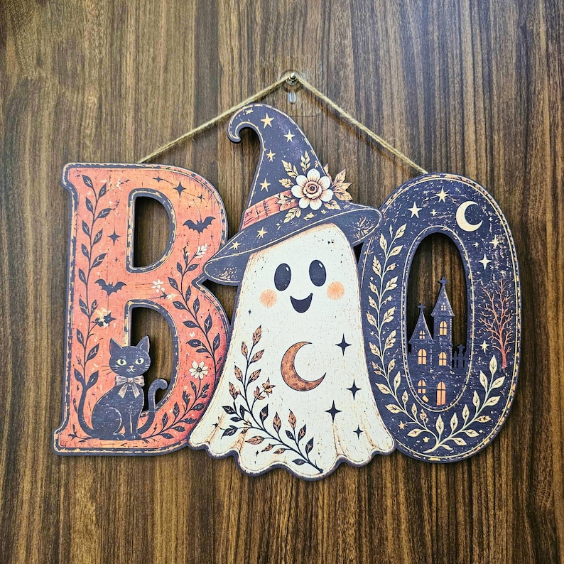 May include: A hanging wall sign spelling BOO with a ghost wearing a witch hat in the center. The letter B features a black cat and floral vines on an orange background. The letter O depicts a dark haunted house, stars, and a crescent moon.