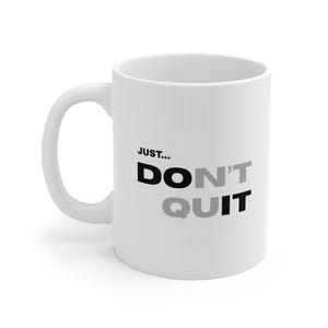 Könnte beinhalten: Ein weißer Keramikbecher mit dem schwarzen und grauen Text "JUST... DO N'T QUIT" auf der Vorderseite. Der Becher hat eine zylindrische Standardform mit einem geschwungenen Henkel auf der linken Seite und bietet ein schlichtes, funktionales Design.