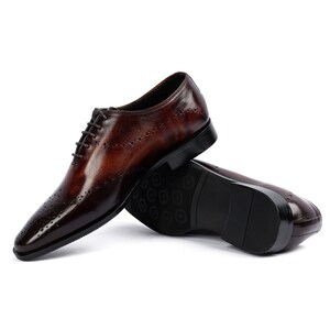 May include: A pair of brown leather lace-up shoes with a brogue pattern. The shoes are on a white background.
