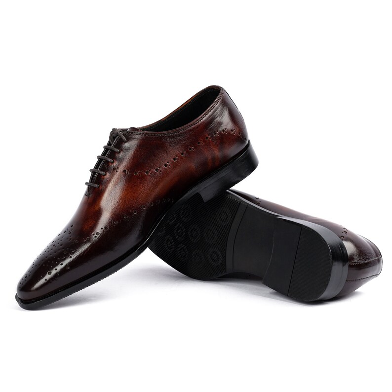 May include: A pair of brown leather lace-up shoes with a brogue pattern. The shoes are on a white background.