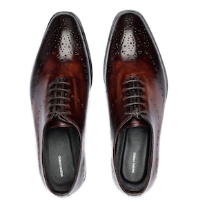 May include: A pair of brown leather lace-up shoes with a brogue design. The shoes have a pointed toe and a black leather sole. The brand name "VALERIO VENETO" is printed on the inside of each shoe.