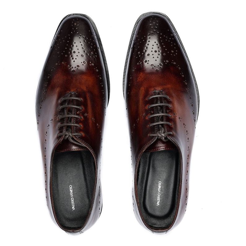 May include: A pair of brown leather lace-up shoes with a brogue design. The shoes have a pointed toe and a black leather sole. The brand name "VALERIO VENETO" is printed on the inside of each shoe.