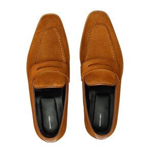 May include: A pair of brown suede loafers with a leather strap across the top. The loafers have a black leather lining and a white "VALENTINO GARAVANI" label on the inside.