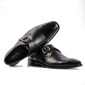 May include: A pair of black leather monk strap shoes with gold buckles. The shoes are on a white background. The brand name "VALERIO VENETO" is visible on the insole of one shoe.