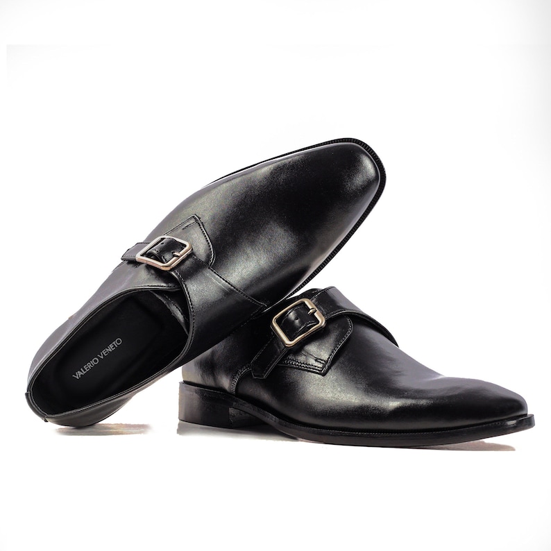 May include: A pair of black leather monk strap shoes with gold buckles. The shoes are on a white background. The brand name "VALERIO VENETO" is visible on the insole of one shoe.