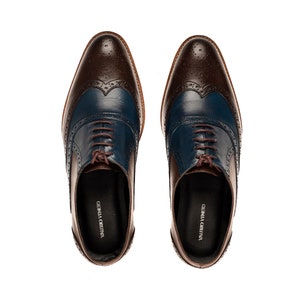 Op de afbeelding: Een paar bruine en blauwe leren veterschoenen met wingtip details. De schoenen hebben een bruin leren bovenwerk met een blauwe leren neus en een bruine leren hak. De schoenen zijn gelabeld "VALENTINO VENETO" en "GIUSEPPE CREATIVA".