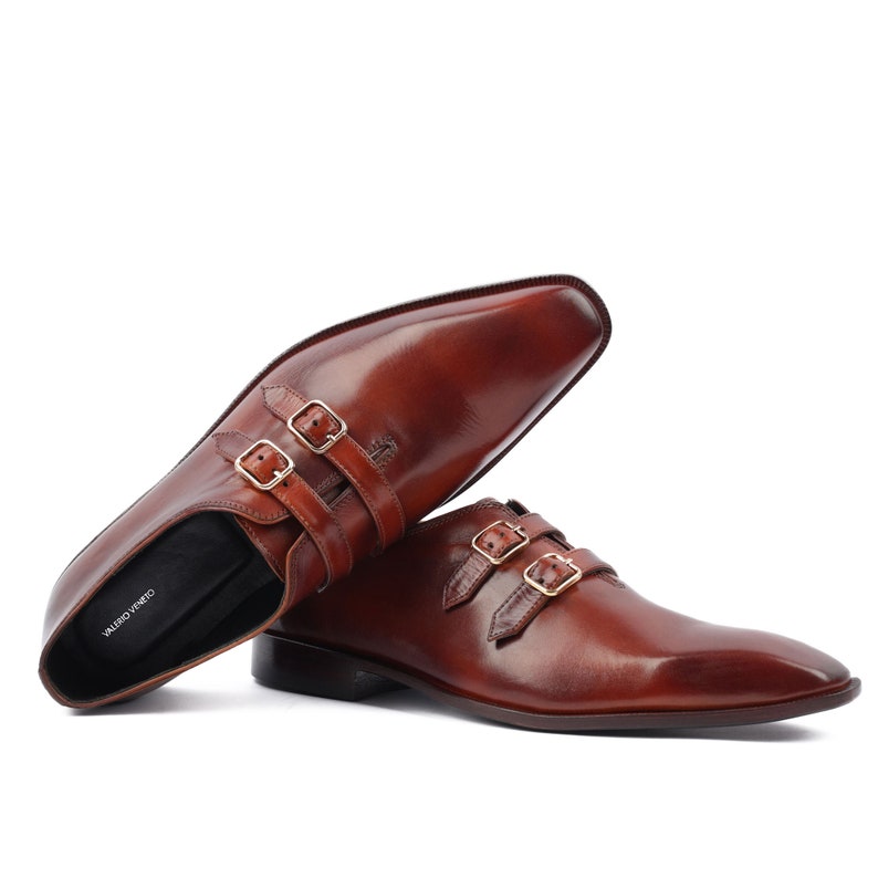 May include: A pair of brown leather dress shoes with three buckles on each shoe. The shoes have a pointed toe and a low heel.