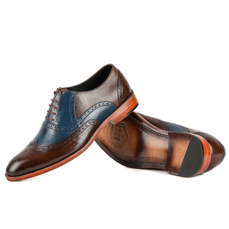 Op de afbeelding: Een paar bruine en blauwe leren brogueschoenen met een wingtip-ontwerp. De schoenen hebben een vetersluiting en een bruine leren zool.