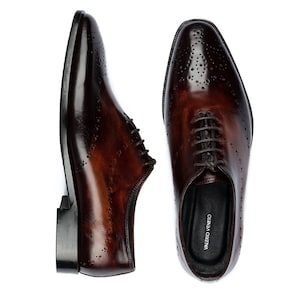 May include: A pair of brown leather lace-up shoes with a perforated design. The shoes have a black leather sole and a black leather lining. The brand name "VALERIO VENETO" is printed on the inside of the right shoe.