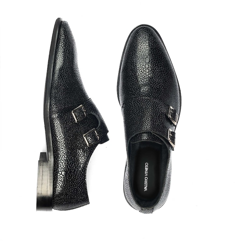 K&ouml;nnte beinhalten: Schwarze Lederschuhe mit doppeltem M&ouml;nchriemen, texturierter Oberfl&auml;che und silbernen Schnallen. Die Schuhe tragen den Markennamen "VALERIO VENETO", der auf der Innenseite aufgedruckt ist.