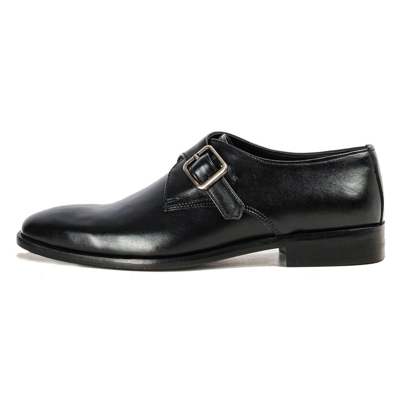 May include: Black leather dress shoes with a single buckle strap. The shoes have a pointed toe and a low heel.